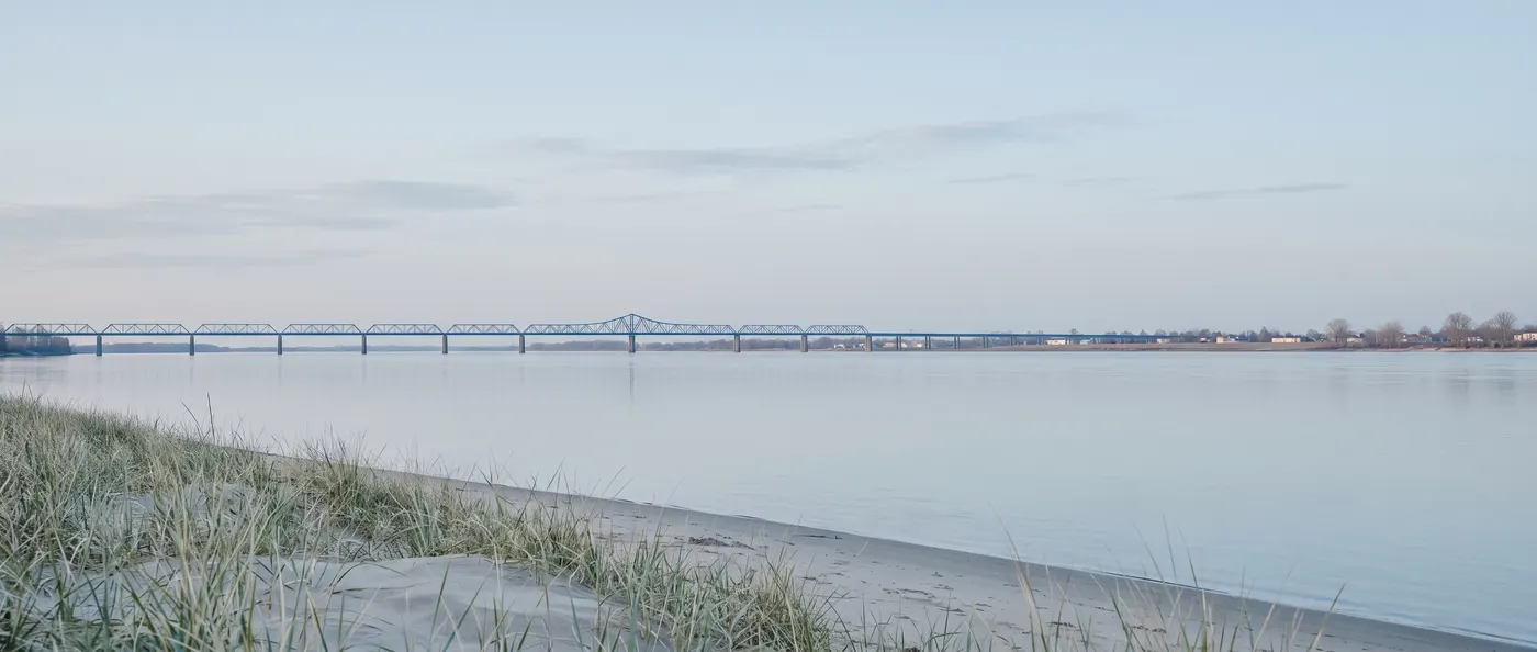 Illustration générée : un fleuve très large et calme au petit matin, un long pont bas sur de nombreuses piles au loin et un ciel pâle